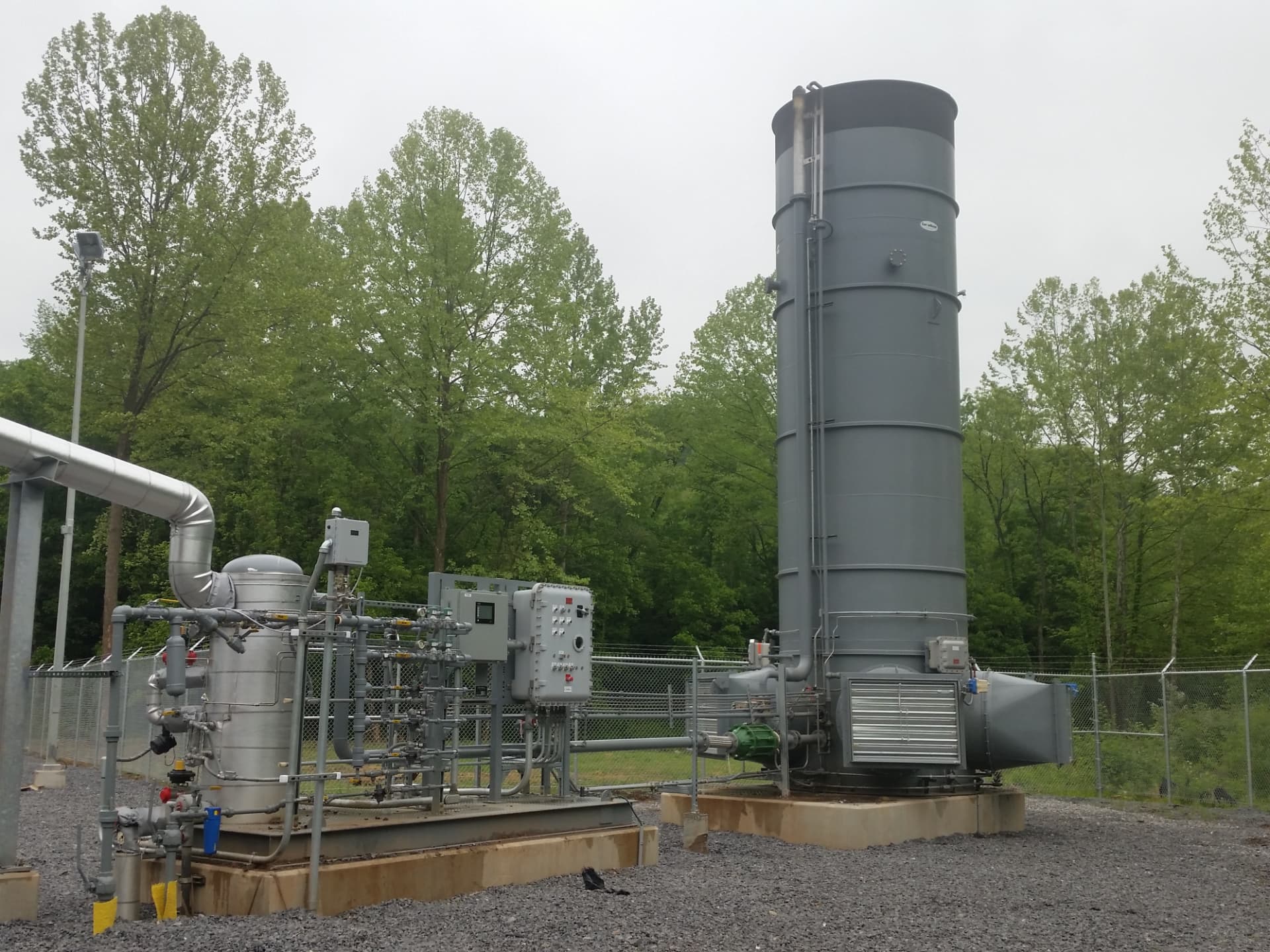 PyroNXT enclosed combustor with control panel and process piping beside a vertical stack