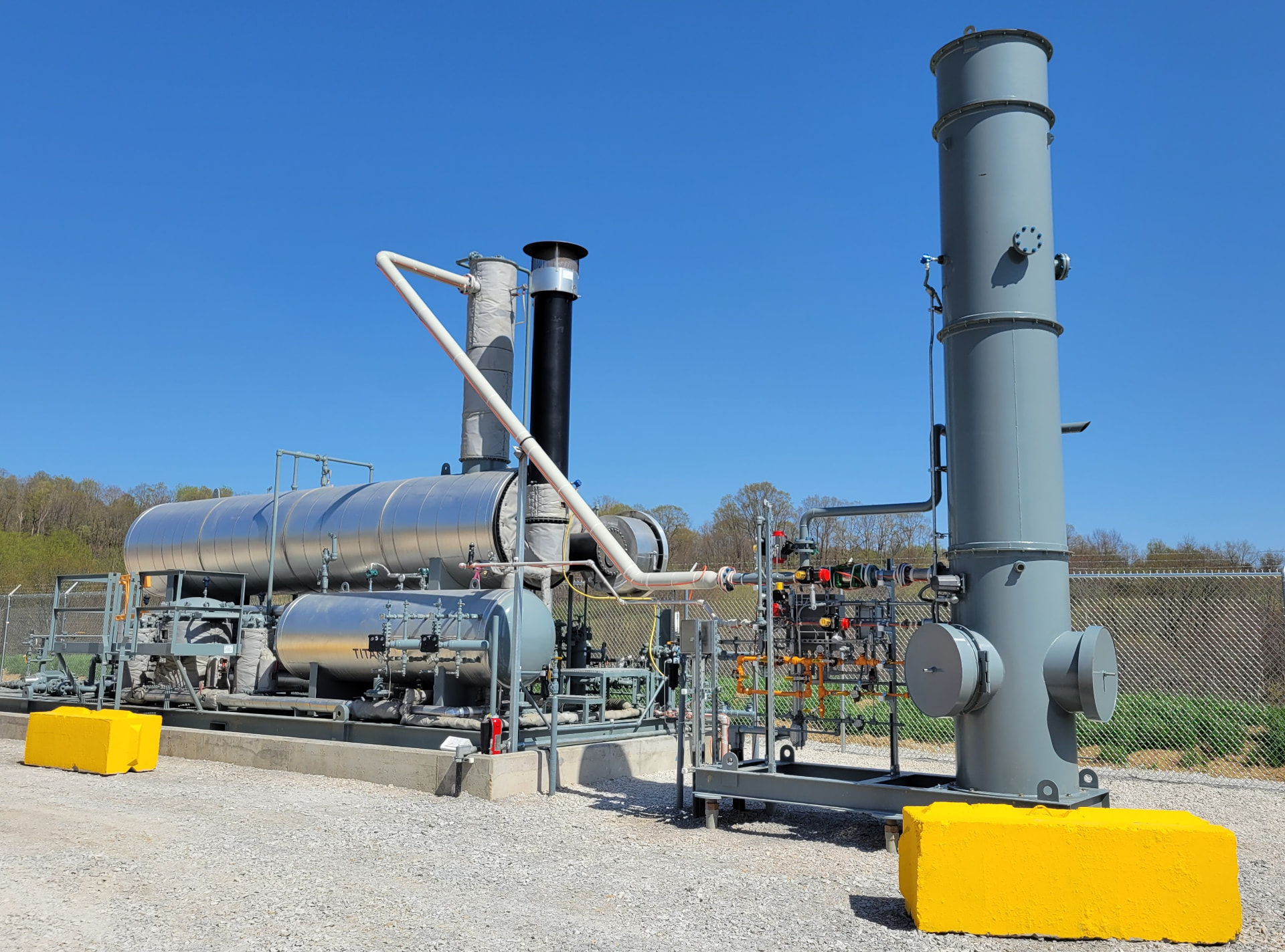 Skid-mounted enclosed combustor system with piping and vertical stack installed on a gravel pad